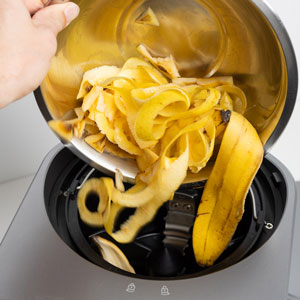 une main verse des épluchures et déchets organiques dans un composteur de cuisine
